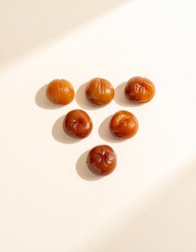 Six glossy candied chestnuts on a pale cream surface, minimal japanese food flat lay with copy space