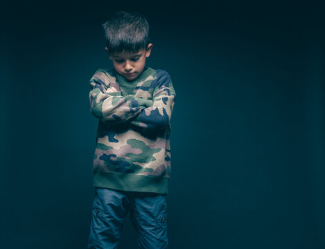 Sad boy standing with arms crossed looking down in studio