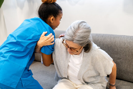 Home health nurse supporting an elderly woman as she rises from a couch, providing compassionate in home care