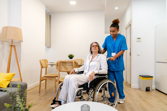 Latina home health nurse guiding an elderly woman in a wheelchair through a bright, comfortable home