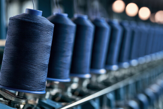 Detailed shot of blue cotton thread spools mounted on a textile machine in a garment factory. The scene shows various spools in different depths of
