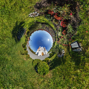 creative tiny planet photo of a rural landscape with dirt road, green fields, and cloudy sky forming a circular world.