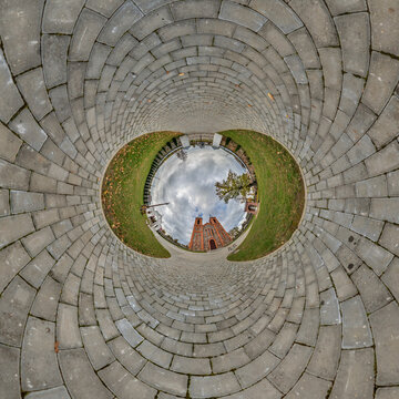 creative tiny planet photo of a rural landscape with dirt road, green fields, and cloudy sky forming a circular world.