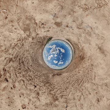 creative tiny planet photo of a rural landscape with dirt road, green fields, and cloudy sky forming a circular world.