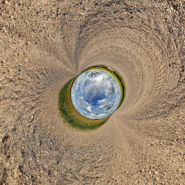 creative tiny planet photo of a rural landscape with dirt road, green fields, and cloudy sky forming a circular world.