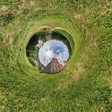 creative tiny planet photo of a rural landscape with dirt road, green fields, and cloudy sky forming a circular world.