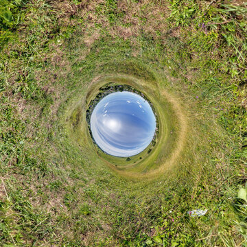 creative tiny planet photo of a rural landscape with dirt road, green fields, and cloudy sky forming a circular world.