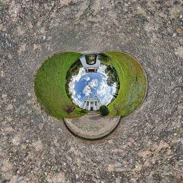 creative tiny planet photo of a rural landscape with dirt road, green fields, and cloudy sky forming a circular world.
