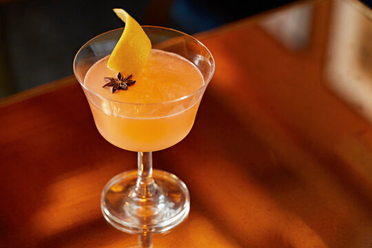 Orange cocktail garnished with star anise and lemon peel