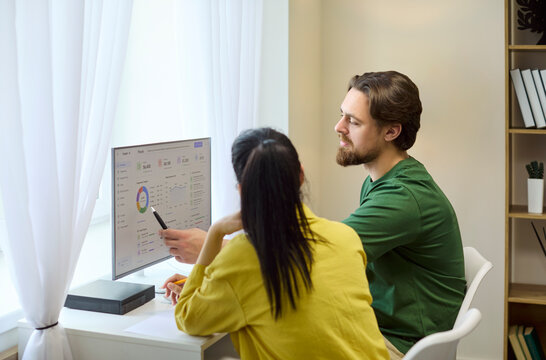 Couple budget planning on a computer dashboard. At a bright home office they review finance charts and analysis, track savings, and discuss expenses. Clear budgeting and teamwork concept.
