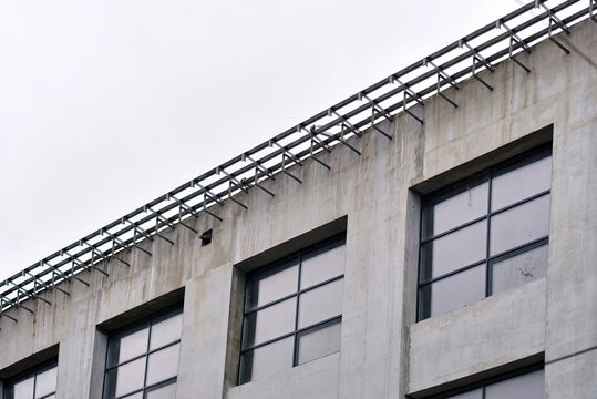Residential or commercial building facade with large glass windows and roofline metal framework during development. Structural metal support brackets and glass windows on upper concrete facade