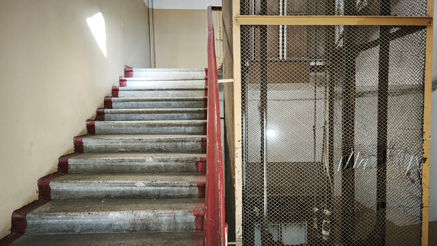 Old concrete staircase and metal mesh elevator shaft inside an industrial building, showing worn architecture, aging infrastructure, urban decay and neglected interior.