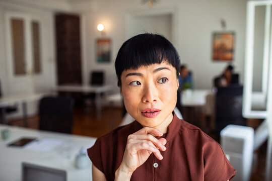Thoughtful woman with hand on chin in office