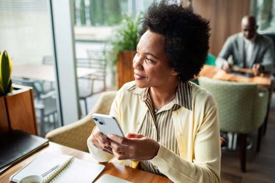 Smiling woman looking away while holding smartphone in cafe
