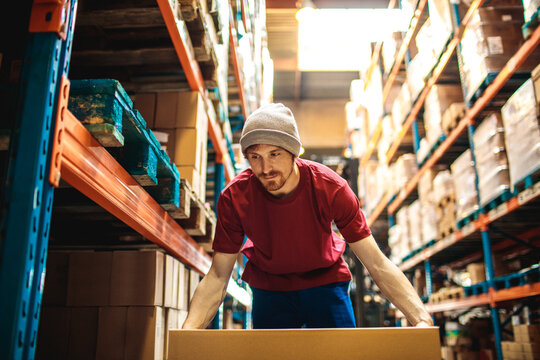 Warehouse worker lifting cardboard box in warehouse aisle