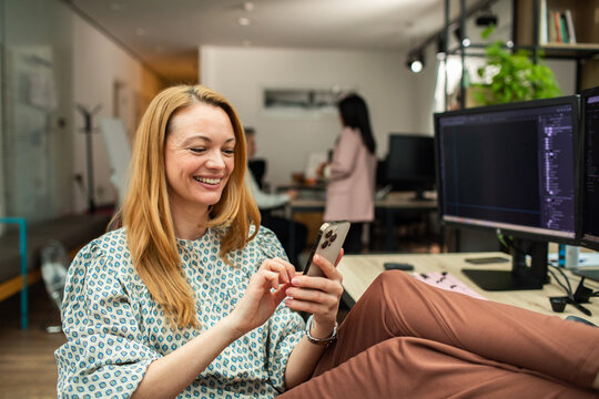 Smiling woman with feet up using smartphone at desk