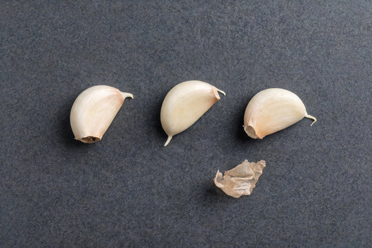 Three garlic cloves with papery skin on a dark surface