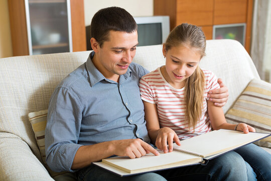 Father and daughter sharing an open notebook on a sofa