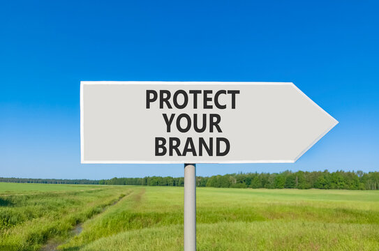Protect your brand words symbol. Concept words Protect your brand on beautiful grey road sign. Beautiful blue sky green grass background. Business and protect your brand concept. Copy space.