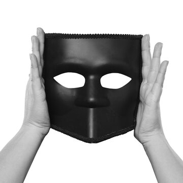 Two hands hold a black face mask with eye openings and a pointed lower edge against a transparent background, with no location or time shown.