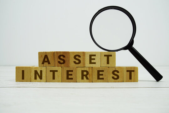 ASSET INTEREST alphabet letters with magnifying glass on wooden background