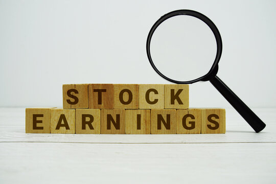 STOCK EARNINGS alphabet letters with magnifying glass on wooden background