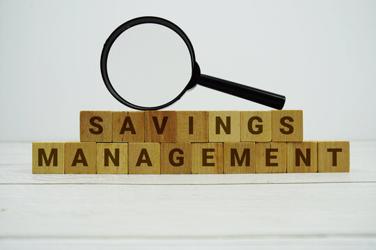 SAVINGS MANAGEMENT alphabet letters with magnifying glass on wooden background