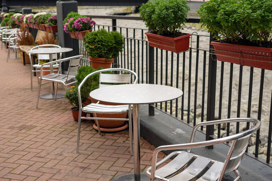 Cozy summer cafe terrace with metal tables and chairs, decorated with vibrant flower pots on the fence