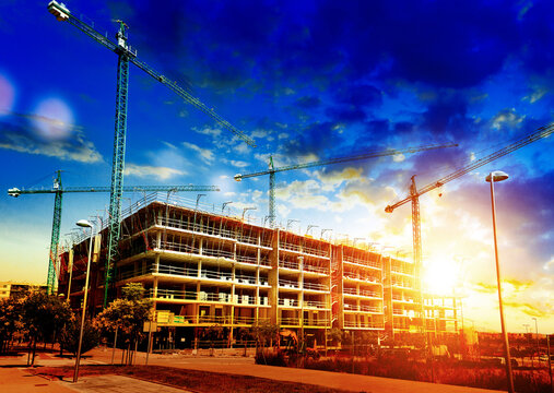  Gr&uacute;as de obra al atardecer con escenario de desarrollo urbano. Gr&uacute;as silueteadas y edificios inacabados contra un colorido cielo al atardecer en una obra en construcci&oacute;n activa. Paisaje industrial 